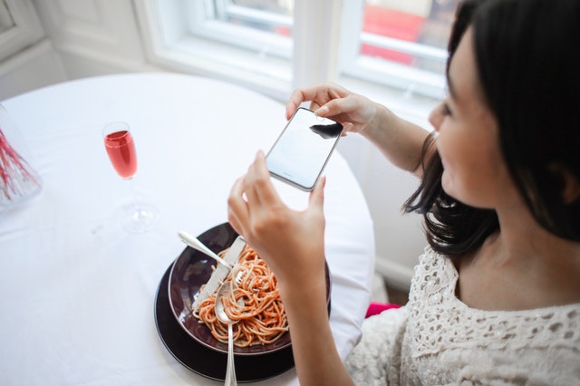 Žena fotografující mobilem jídlo na talíři